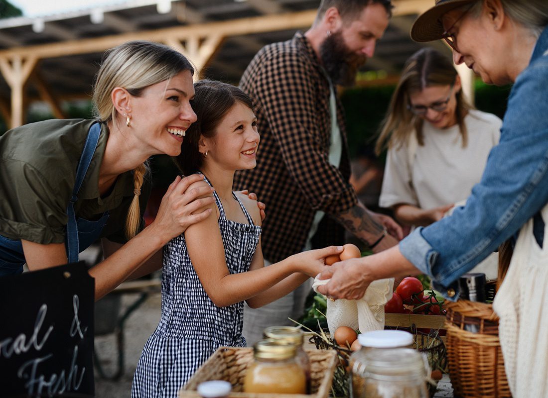 About Our Agency - Happy Mother and Daughter Pay for Eggs at a Farmer's Market