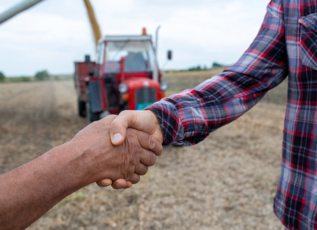 Insurance Solutions - Close-up of Two People Shaking Hands at a Crop Field With a Red Tractor in the Background